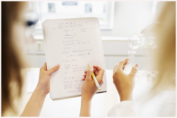Cropped image of female students analyzing formulas while performing experiments in classroom